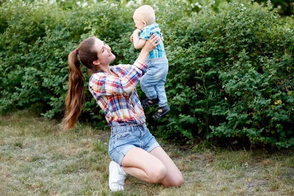 young mom with ponytail holding baby outside