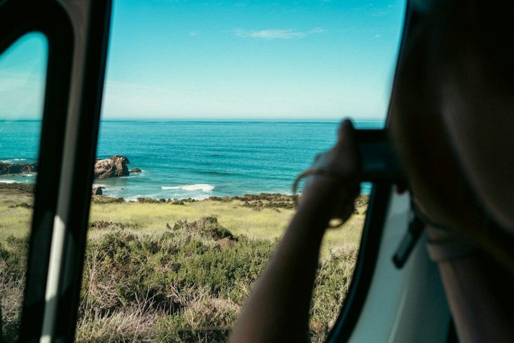 Woman taking picture of ocean from car window